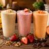 Licuados naturales de plátano, fresa y mamey preparados con leche e ingredientes frescos sobre una mesa de madera rústica.
