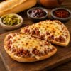 Molletes de longaniza con frijoles refritos y queso manchego gratinado, servidos sobre bolillo recién horneado.