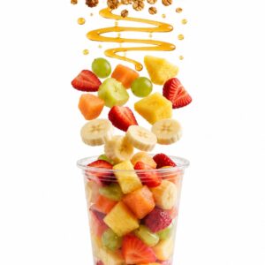 Vaso de fruta fresca con ingredientes flotando: frutas variadas, miel y granola sobre un vaso transparente con fondo blanco.